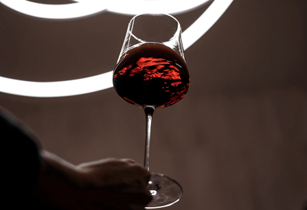 Rotweinglas vor stilisiertem, leuchtendem Hintergrund mit geometrischen Formen.