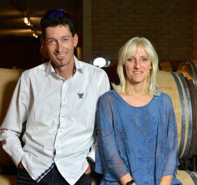 Ein Mann und eine Frau vor hölzernen Weinfässern in einem Keller.