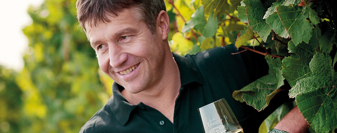 Mann mit Weinglas und Flasche im Weinberg, lächelnd.