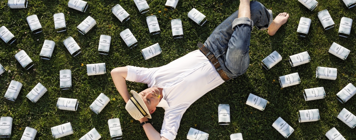 Person im weißen Hemd liegt auf Gras, umgeben von vielen Flaschen.