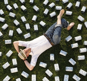 Person im weißen Hemd liegt auf Gras, umgeben von vielen Flaschen.