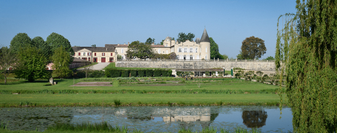 Schloss mit Turm, umgeben von Gärten, Bäumen und einem Teich im Vordergrund.