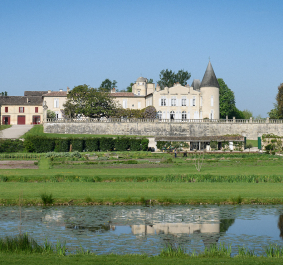 Schloss mit Turm, umgeben von Gärten, Bäumen und einem Teich im Vordergrund.