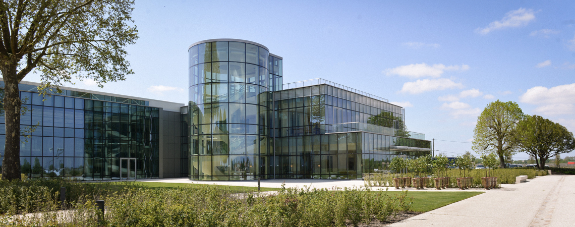 Modernes Gebäude mit großer Glasfassade und runden Türmen, umgeben von Bäumen und Grünflächen.