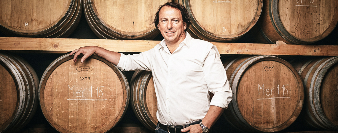 Mann in einem Weinkeller, lehnt an Holzfässern und trägt ein weißes Hemd.