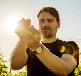 Mann inspiziert Hopfenpflanze im Sonnenlicht, umgeben von Natur.