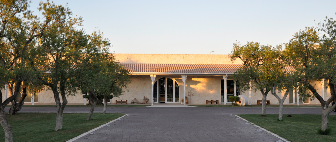 Steinbau mit Ziegeldach, umgeben von Bäumen und Rasenflächen im Abendlicht.