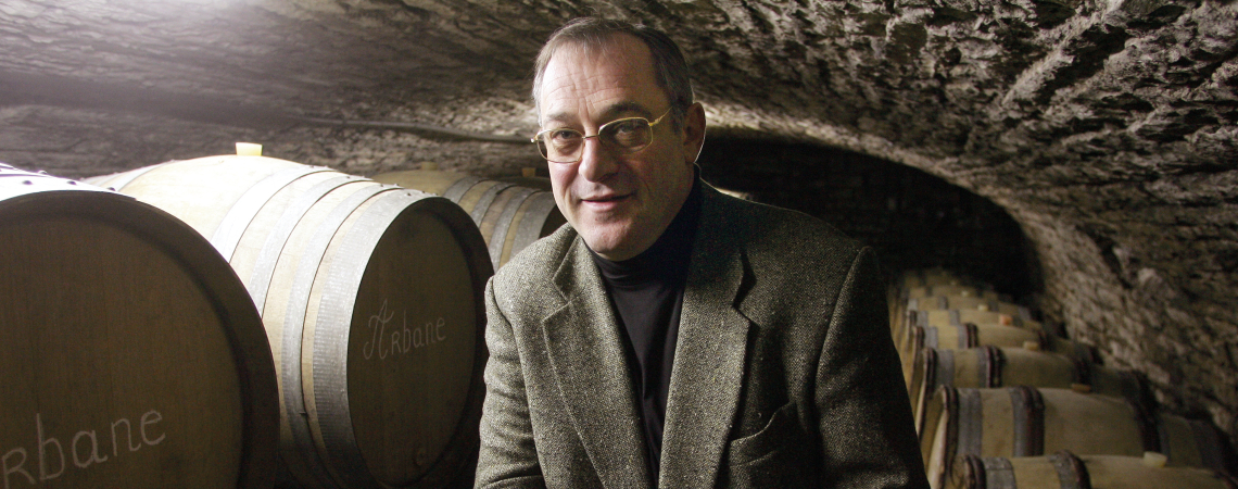 Mann in Weinkeller, umgeben von Holzfässern, trägt graues Sakko.