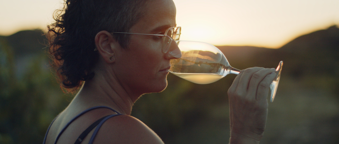 Frau mit Brille und Weinglas bei Sonnenuntergang in der Natur.