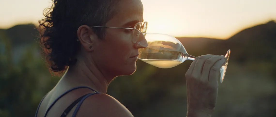 Frau mit Brille und Weinglas bei Sonnenuntergang in der Natur.