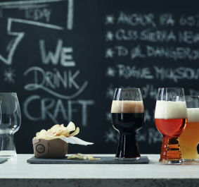 Drei Craft-Biere neben Chips vor einer Tafel mit Kreidezeichnungen.