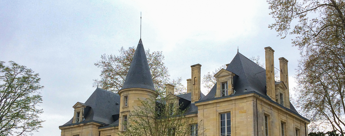 Historisches Schloss mit Türmen und gepflegtem Garten, von Bäumen umgeben.