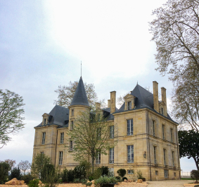 Historisches Schloss mit Türmen und gepflegtem Garten, von Bäumen umgeben.