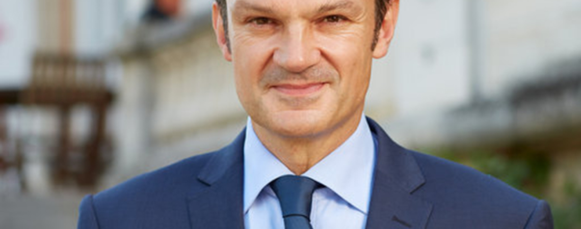 Mann im Anzug mit Sektglas, im Freien, verschwommener Hintergrund.