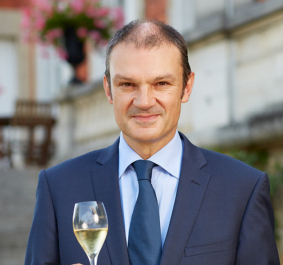 Mann im Anzug mit Sektglas, im Freien, verschwommener Hintergrund.