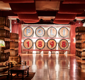 Holzfässer in warm beleuchtetem Raum, gemütliche Sitzecke im Vordergrund.