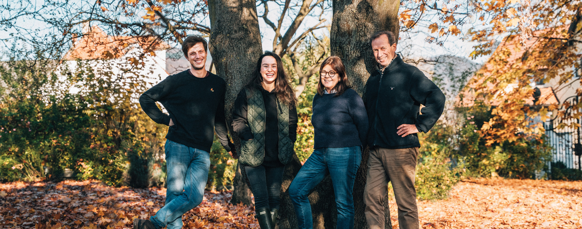 Vier Personen posieren vor einem Baum im herbstlichen Laub.