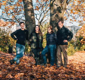 Vier Personen posieren vor einem Baum im herbstlichen Laub.