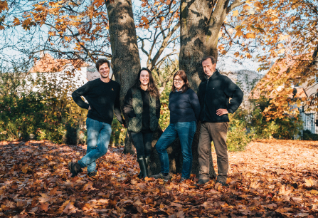 Vier Personen posieren vor einem Baum im herbstlichen Laub.