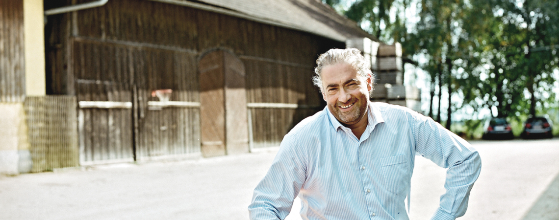 Mann in weißem Hemd sitzt auf Kiste mit Äpfeln vor Scheune.