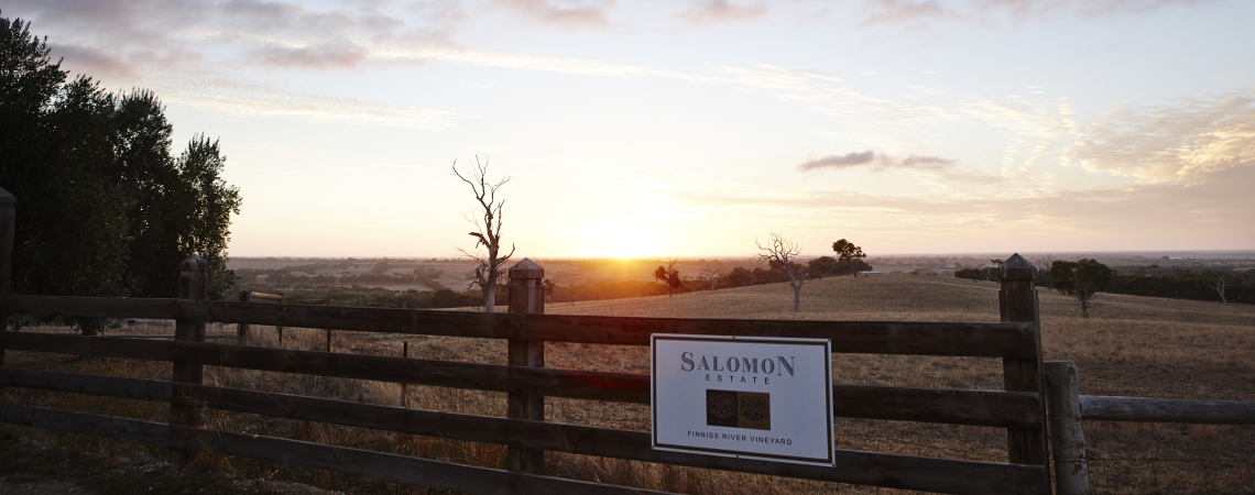 Sonnenuntergang über weitläufiger Landschaft mit Holzzaun im Vordergrund.