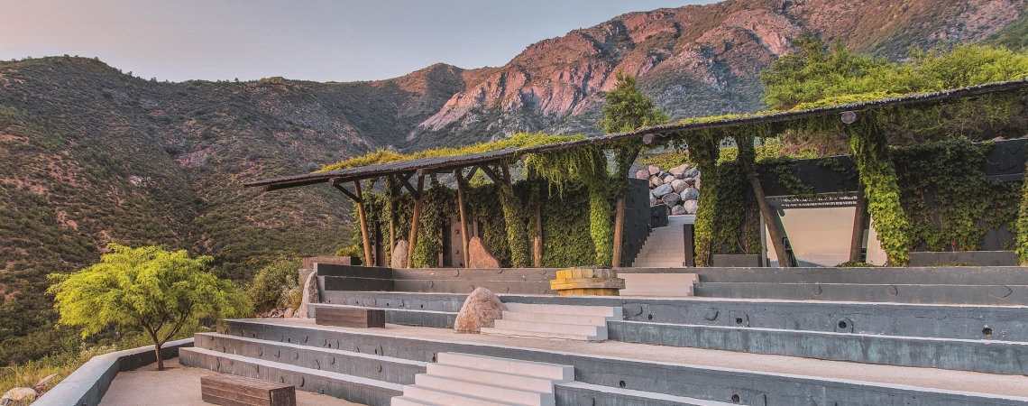 Terrasse mit Stufen und Pflanzen, umgeben von Bergen bei Sonnenuntergang.