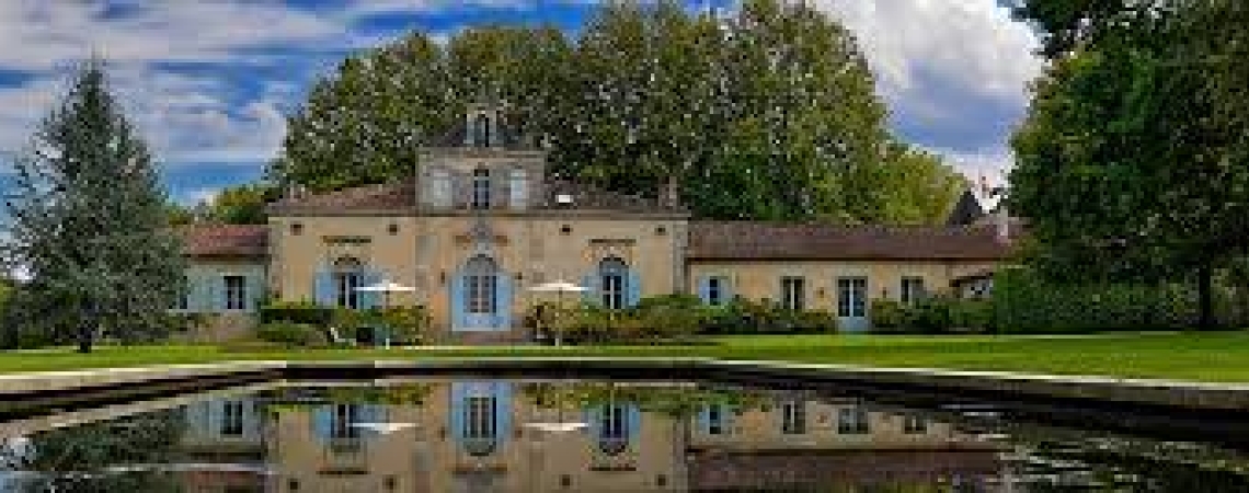 Historisches Gebäude mit symmetrischer Fassade, vor einem reflektierenden Teich und grünen Bäumen.