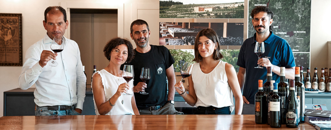 Fünf Personen beim Weinverkosten, stehend hinter einem Tisch mit Weinen.