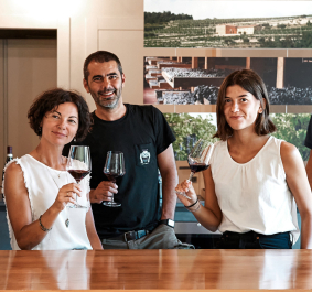 Fünf Personen beim Weinverkosten, stehend hinter einem Tisch mit Weinen.