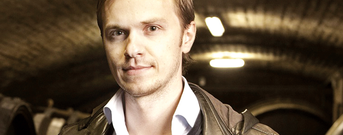 Mann in brauner Lederjacke steht in einem stimmungsvoll beleuchteten Weinkeller.