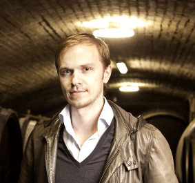 Mann in brauner Lederjacke steht in einem stimmungsvoll beleuchteten Weinkeller.