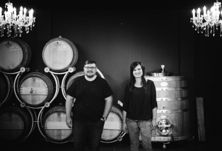 Zwei Personen vor Weinfässern und Kronleuchtern in einem Weinkeller.