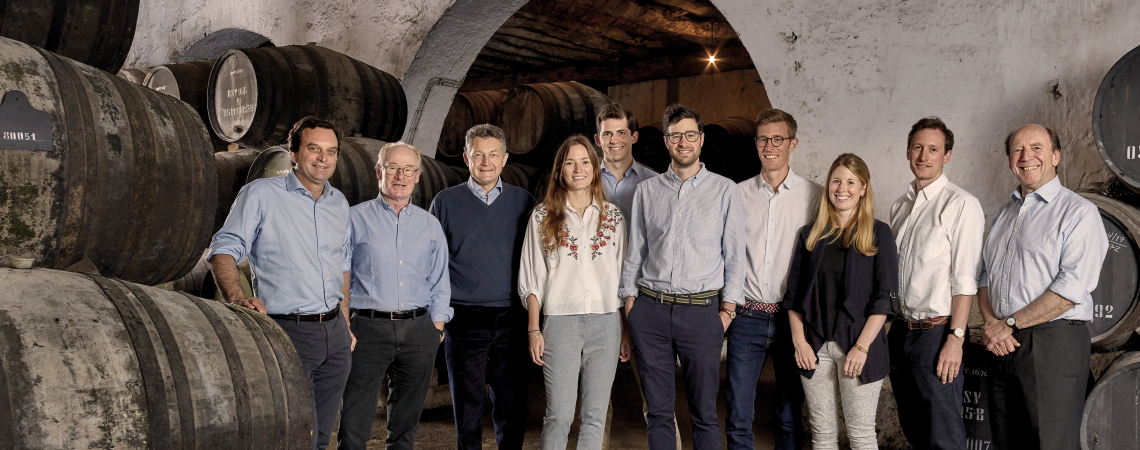 Gruppe von Menschen in einem Weinkeller, umgeben von großen Holzfässern.