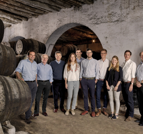 Gruppe von Menschen in einem Weinkeller, umgeben von großen Holzfässern.