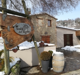 Rustikales Steingebäude mit Holzfass und schneebedecktem Hof bei winterlicher Landschaft.