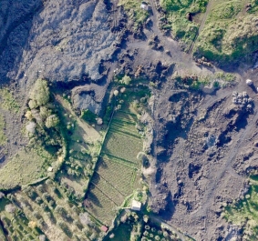 Luftaufnahme von grünen Feldern neben dunkler, zerklüfteter Landschaft.