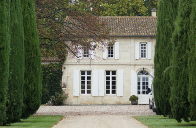 Elegantes Landhaus mit weißen Fensterläden, flankiert von hohen Zypressen.