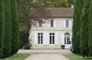 Elegantes Landhaus mit weißen Fensterläden, flankiert von hohen Zypressen.
