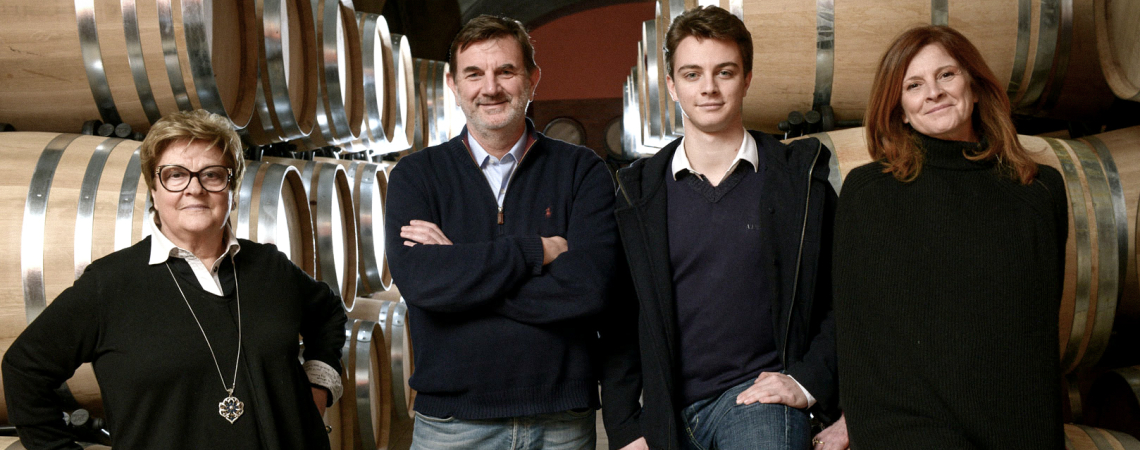 Vier Personen posieren vor hölzernen Weinfässern in einem Kellerraum.