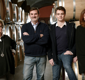 Vier Personen posieren vor hölzernen Weinfässern in einem Kellerraum.