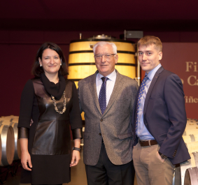 Drei Personen vor Weinfässern in stilvollem, elegantem Ambiente.