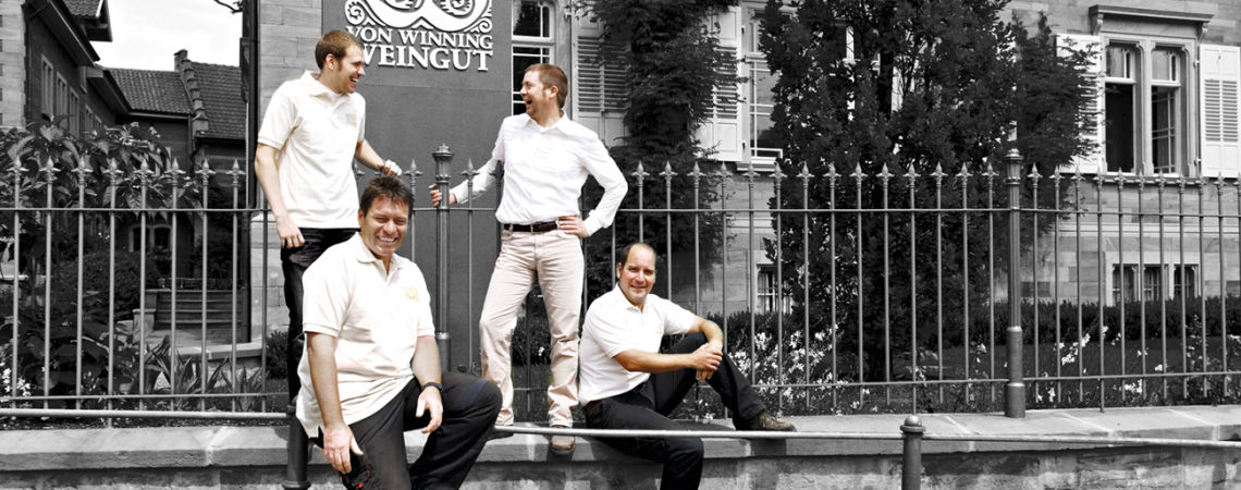 Vier Männer in weißen Hemden vor traditionellem Gebäude, schwarz-weiß mit Highlight auf Personen.