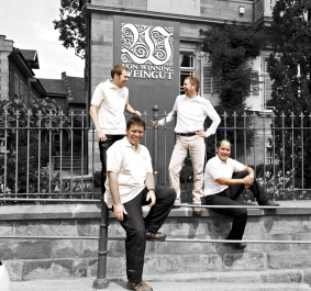 Vier Männer in weißen Hemden vor traditionellem Gebäude, schwarz-weiß mit Highlight auf Personen.