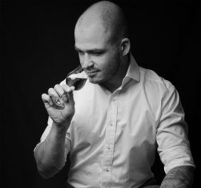 Mann in Hemd genießt Drink, sitzt auf Fass, hält Flasche.