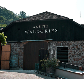 Historisches Weingut aus Stein mit Holzverkleidung, umgeben von grüner Landschaft.