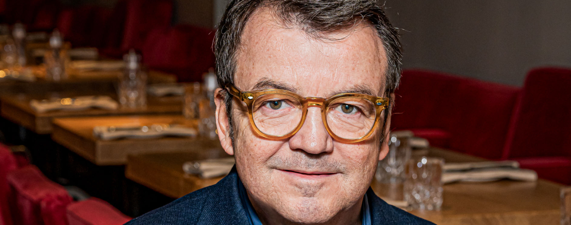 Mann in blauem Blazer sitzt in stilvollem Restaurant mit roten Stühlen.