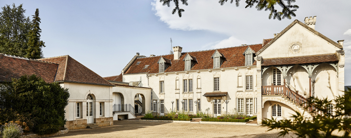 Historisches Herrenhaus mit weißen Fassaden, rotem Dach und großer gepflasterter Einfahrt.