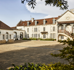 Historisches Herrenhaus mit weißen Fassaden, rotem Dach und großer gepflasterter Einfahrt.