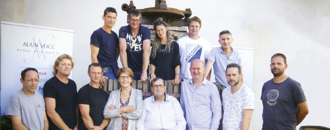 Gruppe von 13 Personen posiert vor einer Weinpresse im Freien.