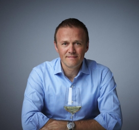 Mann in blauem Hemd mit Weinglas vor neutralem Hintergrund.